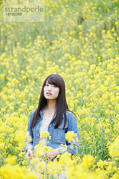 Junge Japanerin blickt in einem Blütenfeld in die Kamera