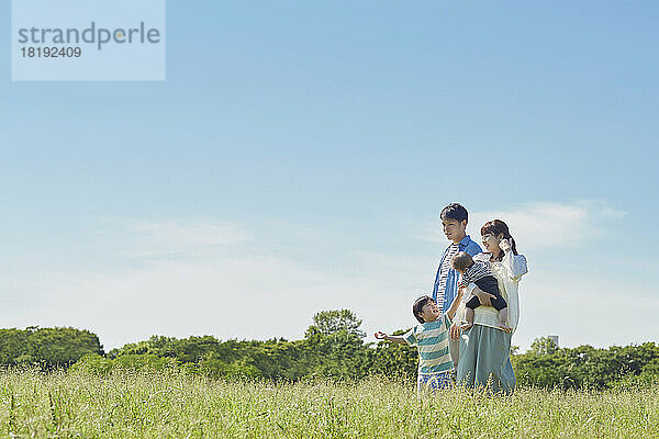 Japanische Familie lächelt mit blauem Himmel im Hintergrund