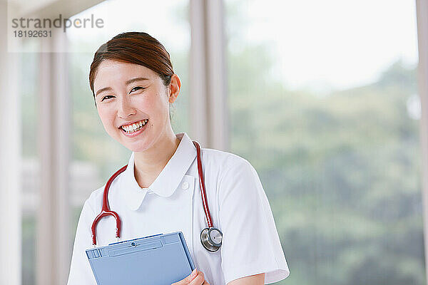 Lächelnde junge japanische Krankenschwester  die durch den Flur geht