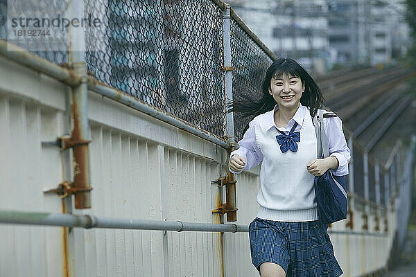 Lächelndes japanisches Highschool-Mädchen auf der Fußgängerbrücke