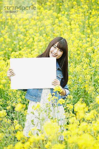 Japanerin hält eine weiße Tafel in einem Blumenfeld