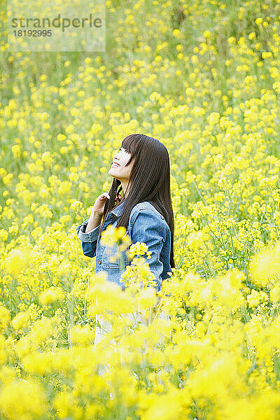 Eine junge Japanerin blickt in einem Blütenfeld in den Himmel