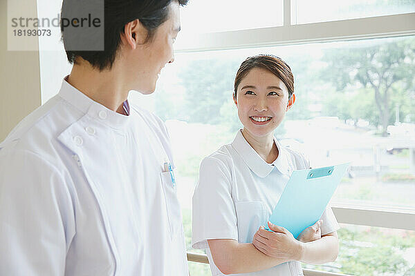 Lächelnde junge japanische Krankenschwester bei einem Gespräch im Flur