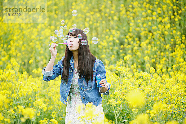 Junge Japanerin bläst Seifenblasen in ein Blütenfeld