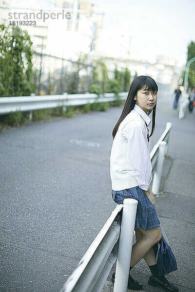 Japanisches Highschool-Mädchen sitzt auf der Leitplanke