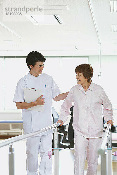 Lächelnde ältere Japanerin und junger Krankenpfleger in der Reha-Einrichtung