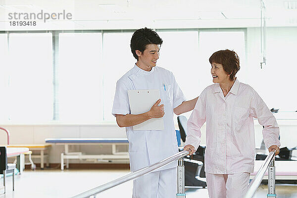 Lächelnde japanische Seniorin und junger Krankenpfleger in der Reha-Einrichtung