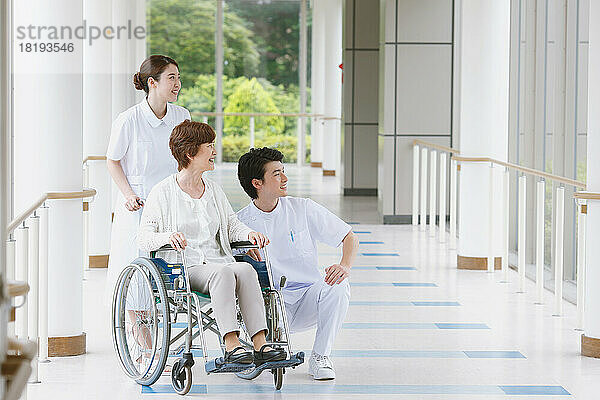 Japanische Seniorin im Rollstuhl und zwei junge Krankenschwestern im Flur