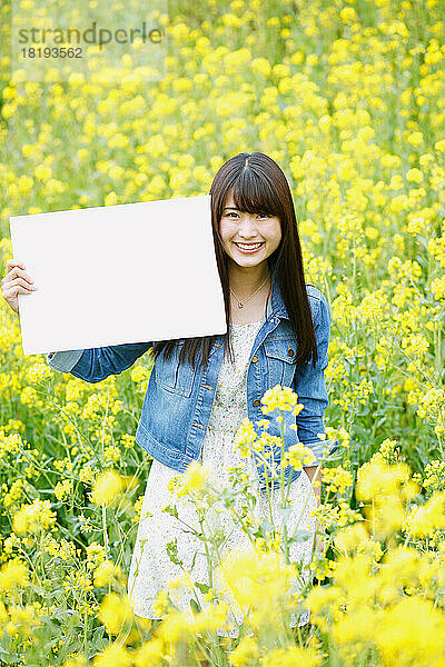 Japanerin hält eine weiße Tafel in einem Blumenfeld