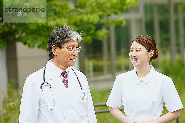 Lächelnder Arzt und eine junge Krankenschwester unterhalten sich im Freien