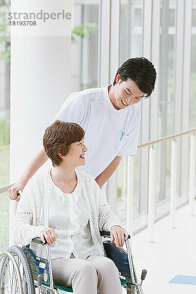 Eine ältere Japanerin im Rollstuhl und ein junger Krankenpfleger unterhalten sich auf dem Flur