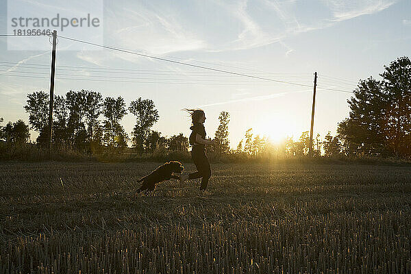 Unbekümmertes Mädchen und Hund laufen in sonnigen ländlichen Bauernhof Feld bei Sonnenuntergang