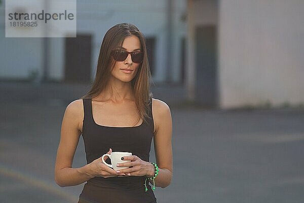 Nettes Mädchen in sonnigen Tag auf Hinterhof mit Tasse Kaffee in der Hand. Kontrastarmes Foto