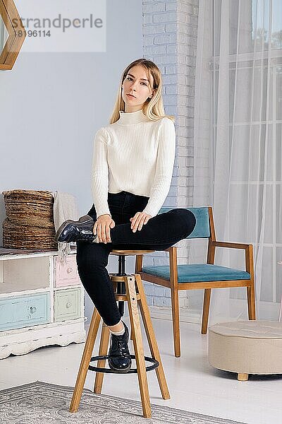 Ganzkörperporträt eines jungen Mädchens auf einem Stuhl im Wohnzimmer sitzend