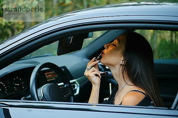 Stilvolle Frau trägt Lippenstift auf  während sie im Auto sitzt