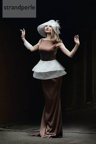 Unauffälliges Porträt eines blonden Mädchens in Seidenkleid mit Baske und modischem Hut mit breiter Krempe