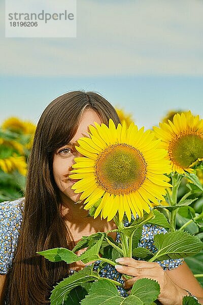 Lustige junge Frau  die ihr halbes Gesicht mit einer Sonnenblume versteckt