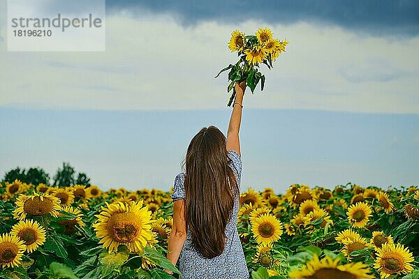 Rückansicht einer Frau mit Sonnenblumenstrauß. Junge Frau mit Sonnenblumen in der Hand streckt den Himmel aus