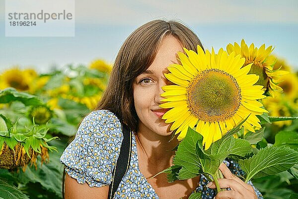 Fröhliche junge Frau  die ihr halbes Gesicht mit einer Sonnenblume verdeckt