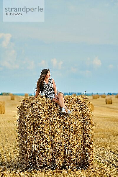 Ruhige junge Frau sitzt auf einem Strohhaufen auf dem Feld