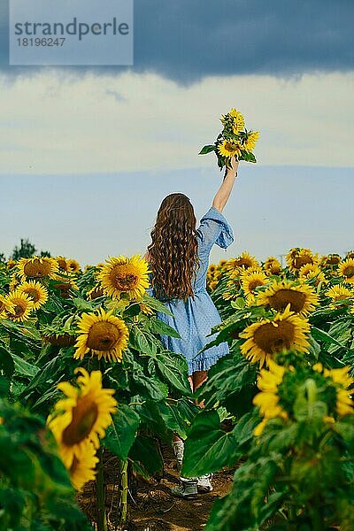 Rückansicht einer Frau mit Sonnenblumenstrauß. Junge Frau mit Sonnenblumen in der Hand streckt den Himmel aus