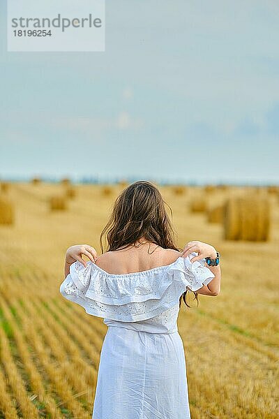 Rückansicht einer jungen Frau  die sich auf dem Feld das Sommerkleid von den Schultern nimmt