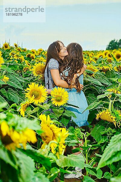 Zwei Freundinnen umarmen sich auf einem Sonnenblumenfeld