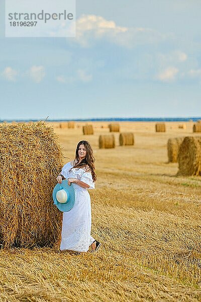 Charmante Frau lehnt sich an einen riesigen Strohballen auf dem Feld in der Sonne