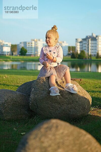 Niedliches kleines Kind sitzt auf Stein in Sonnenuntergang Zeit