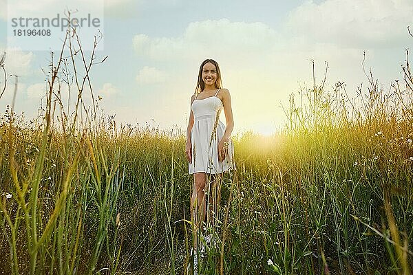 Schöne junge Frau in weißem Kleid zu Fuß auf dem Feld über den Sonnenuntergang