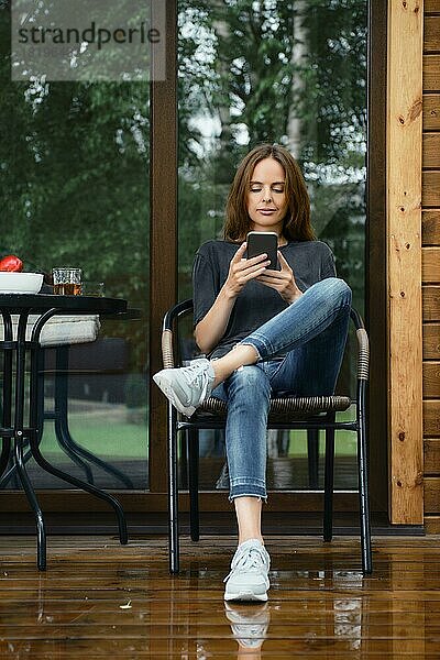Frau  die auf der Terrasse einer Holzhütte sitzt und prüft  was online ist