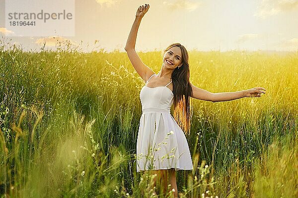 Schöne junge Frau tanzt auf dem Feld über dem Sonnenuntergang