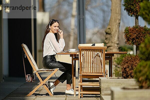 Schöne junge Frau sitzt auf der Terrasse des Cafés in sonnigen Tag und essen Kuchen. Frau genießt erste Frühlingssonne im Freien