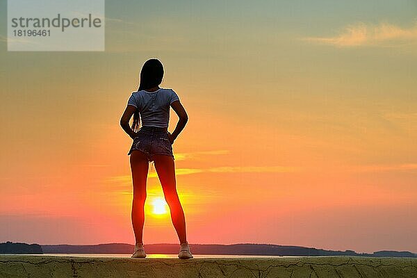 Rückansicht einer Silhouette einer jungen Frau  die bei Sonnenuntergang auf einem Pier steht