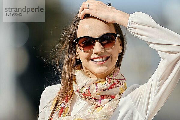 Closeup Stadt Porträt der lächelnden jungen Frau mit Sonnenbrille in windigen Tag