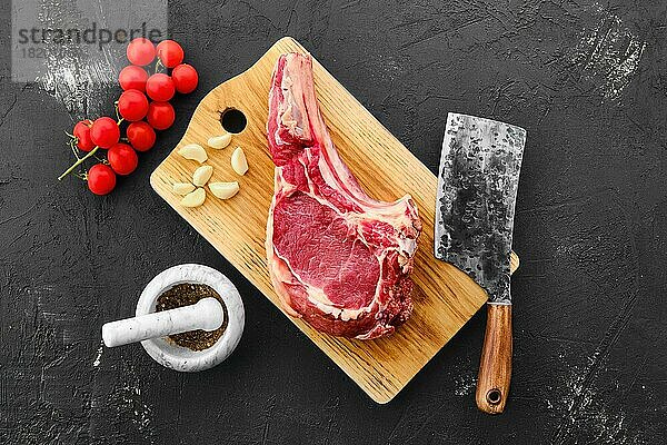 Draufsicht auf Rinder-Ribeye-Steak mit Knochen und Gewürzen auf schwarzem Hintergrund