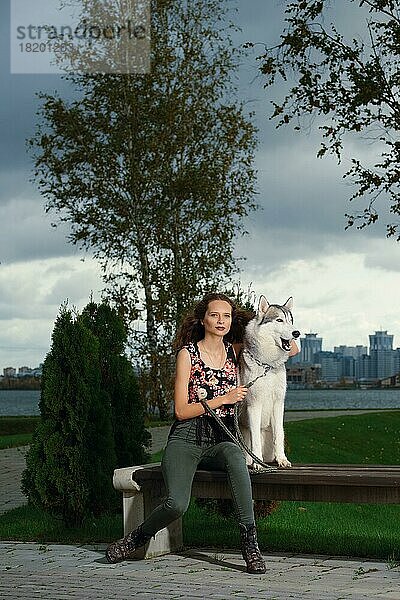 Mädchen mit Husky-Hund im Stadtpark sitzend. Hund auf einer Bank
