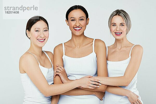 Glückliche asiatische  kaukasische und afrikanische junge Frauen mit verschiedenen Hauttypen in weißen Höschen und Hemd