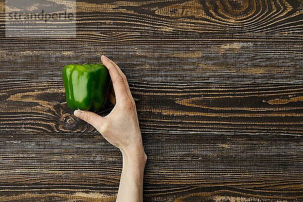 Draufsicht auf eine frische grüne Paprika in den Händen über einem hölzernen Hintergrund