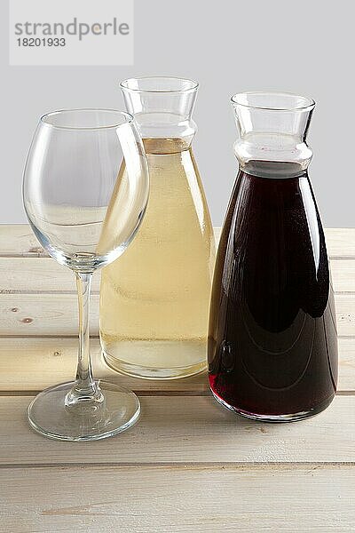 Weinglas und zwei Krüge mit Rot- und Weißwein auf Holztisch