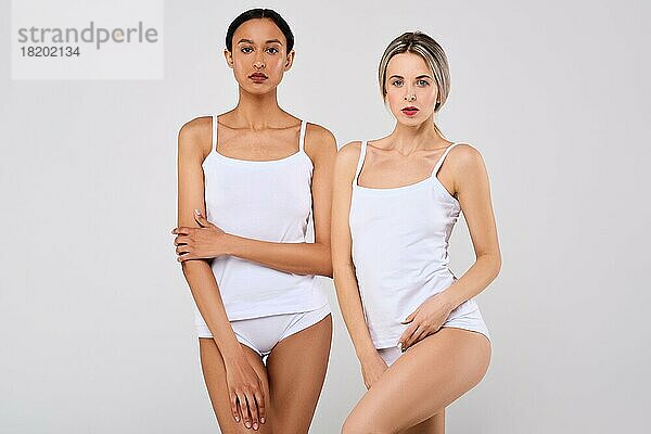 Zwei hübsche kaukasische und afrikanische junge Frauen mit gesunder Haut in weißen Höschen und Hemd