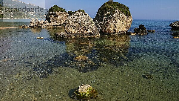 Banana Beach  vorgelagerte kleine Felsen im Meer  grün bewachsen  Meer grün und kristallklar  kleine Felsen unter Wasser sichtbar  wolkenloser blauer Himmel  Insel Zakynthos  Ionische Inseln  Griechenland  Europa