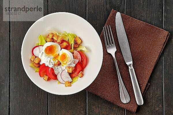Draufsicht auf Salat mit frischer Tomate  Radieschen  gekochtem Ei und Crouton auf dunklem Holztisch