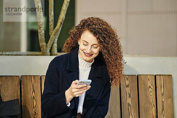 Glückliche junge Frau mit Smartphone im Freien