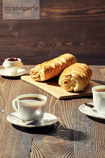 Brötchen und Kaffee auf einem Holztisch im morgendlichen Sonnenlicht. Foto mit geringer Schärfentiefe