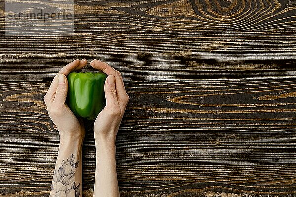 Draufsicht auf eine frische grüne Paprika in den Händen über einem hölzernen Hintergrund