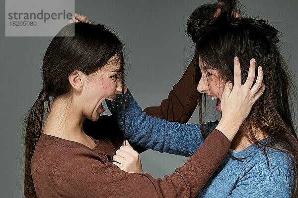 Kokettes Mädchen spielt mit dem Haar ihrer Schwester und macht das Haar wild und unordentlich