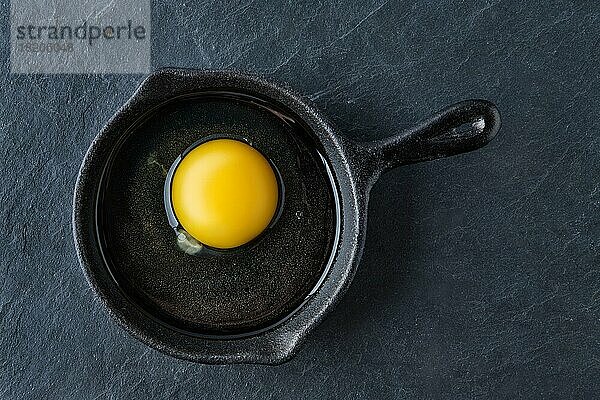 Draufsicht auf ein rohes  ungekochtes Ei in einer kleinen gusseisernen Pfanne