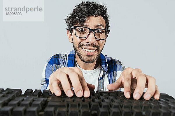 Porträt von nerdy Mann vor der Tastatur  Fröhlich nerdy Kerl mit Händen auf der Tastatur. Lustige nerdy Person vor der Tastatur lächelnd in die Kamera