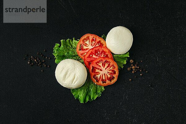 Draufsicht auf Mozzarella mit Scheiben von frischen Tomaten auf schwarzem Hintergrund